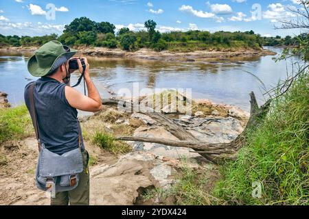 Ein Fotograf mit grünem Hut fotografiert die Savanne auf dem Hintergrund des Flusses in masai Mara, Kenia. Das Konzept einer afrikanischen Walking safar Stockfoto