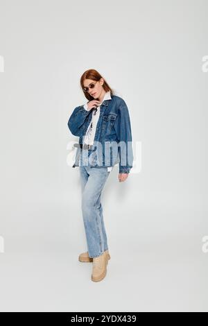 Ein Teenager mit auffälligen langen roten Haaren posiert selbstbewusst in einem stylischen Denim-Outfit in einem Studio. Stockfoto