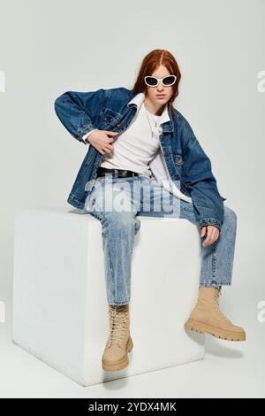 Ein Teenager mit auffälligen roten Haaren präsentiert seine Denim-Mode in einem lebendigen Studio-Setting. Stockfoto