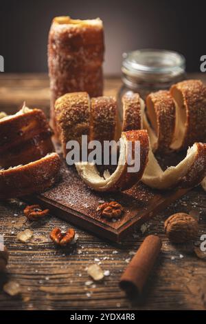 Köstliche, frisch gebackene Chimney-Kuchenrollen, mit Zucker überzogen und begleitet von Walnüssen, ruhen Sie auf einem rustikalen Holztisch aus Stockfoto