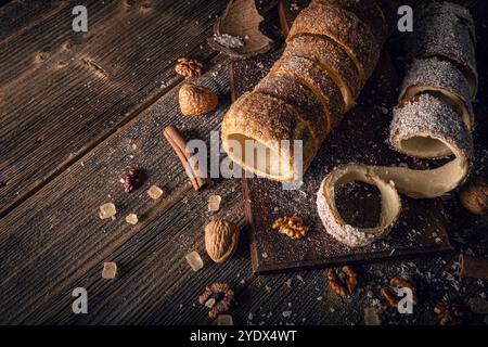 Frisch gebackener Schornsteinkuchen auf Holzbrett mit Walnüssen, braunem Zucker und Zimtstangen für eine gemütliche und köstliche Szene Stockfoto