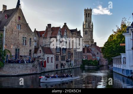 Glockenturm von Brügge, mittelalterliche Backsteinbauten, Kreuzfahrtschiffe und ihre Reflexion auf dem Dijver-Kanal in der Abenddämmerung, vom Rosenkranzquay in Brügge, Belgien. Stockfoto