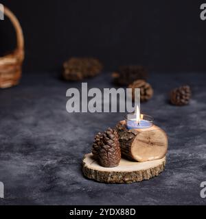 Rustikaler Kerzenhalter mit Tannenzapfen auf Holzscheibe - gemütliche Wohnkultur für Herbst und Winter* Stockfoto