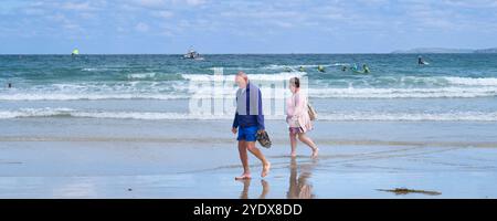 Ein Panoramablick einer Gruppe reifer Urlauber, die barfuß an der Küste von Towan Beach an der Küste von Newquay in Cornwal spazieren Stockfoto