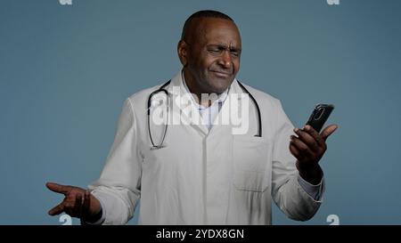 Verärgert frustrierte afroamerikaner Mann Doktor liest schlechte medizinische Nachrichten auf Handy in blauem Hintergrund erhalten Benachrichtigung besorgt männliche Gesundheit Stockfoto