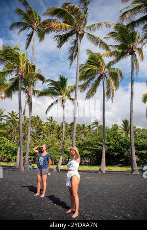 In diesem berührenden Bild stehen eine Mutter und ihre Tochter zusammen am schwarzen Sand des Punalu'u Beach und blicken auf den weiten Horizont. Stockfoto