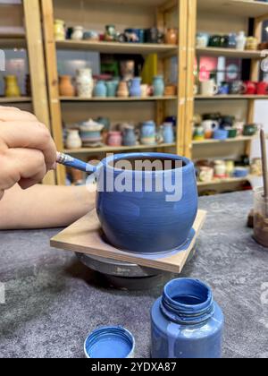 Der Prozess des Malens einer Tonvase während eines Keramikmeisterkurses. Handwerkskunst und Kreativität in Aktion. Die Vase ist mit blauer Glasur bedeckt, Creati Stockfoto