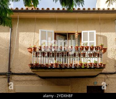 Blick auf ein mediterranes Ferienhaus im ersten Stock mit offenen Fensterläden und Balkon mit vielen Pflanztöpfen. Stockfoto