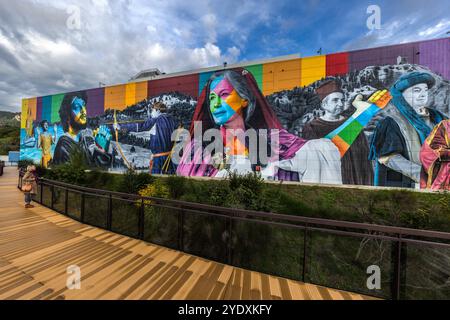 Ein Wandgemälde des brasilianischen Künstlers Eduardo Kobra trägt den Titel „die Geschichte von San Marino“. Die farbenfrohe Darstellung historischer Persönlichkeiten und Szenen befindet sich inmitten der hügeligen Landschaft San Marinos auf einer großen Fläche an der Fassade einer Verpackungsfabrik. Im Hintergrund erheben sich die drei ikonischen Türme im historischen Zentrum von San Marino und bilden im Gegensatz zum modernen Gebäude den perfekten Rahmen für die historische Darstellung auf dem modernen Riesengemälde. Ein Regenbogen am Himmel über dem Gebäude verleiht der Situation einen magischen Moment. Strada del Sabattino, San Marino Stockfoto