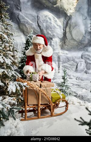 Jolly Santa organisiert farbenfrohe Geschenke auf seinem Schlitten an schneebedeckten Bäumen. Stockfoto