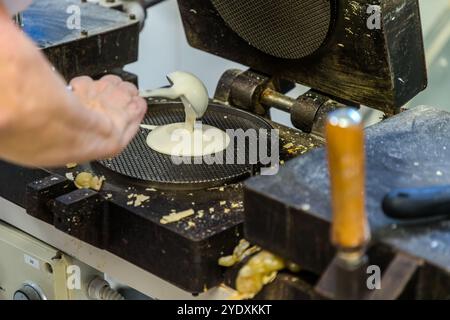 Ein Angestellter von La Serenissima gießt Teig auf ein Waffeleisen. Die Gebrauchsspuren zeigen, dass es sich dabei immer noch um die erste Generation von Waffeleisen handelt, mit denen 1942 die industrielle Produktion begann. Via XXV Marzo, Domagnano, San Marino Stockfoto