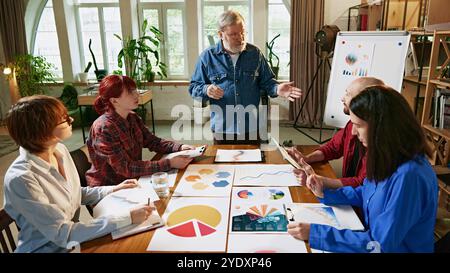 Ältere Teamleiter verwenden visuelle Daten, Diagramme und Diagramme auf dem Whiteboard, um Geschäftsstrategien während der Teambesprechung zu erläutern Stockfoto