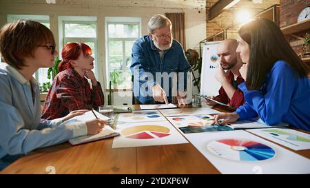 Erfahrene Führungskräfte und junge Fachkräfte arbeiten bei der strategischen Planung zusammen und stellen Teamarbeit und Innovation im Geschäftsumfeld vor. Stockfoto
