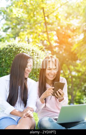 Asiatische Frau, die im grünen Park sitzt und einen Laptop benutzt. Frau, die an einem Laptop arbeitet, glückliches Unternehmerunternehmen, das ein Notebook verwendet, während die Hände auf der Tastatur tippen Stockfoto