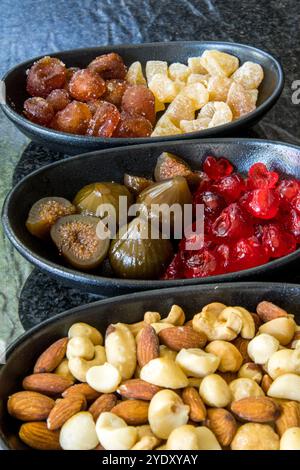 Schwarze Wüstenschalen gefüllt mit verschiedenen Arten von Konserven und einer Mischung von Nüssen. Stockfoto