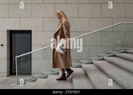 Geschäftsfrau, die in einem Business Center Treppen hinabsteigt und an einem hellen Tag einen Laptop mit sich trägt Stockfoto