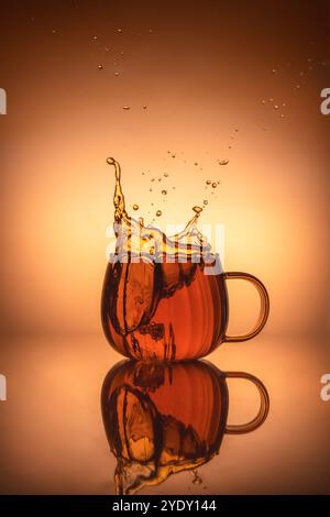 Kreative Splash-Fotografie in transparentem Becher mit Tee, warmen orangen Farben, mit Kopierraum, Komposition Stillleben Stockfoto