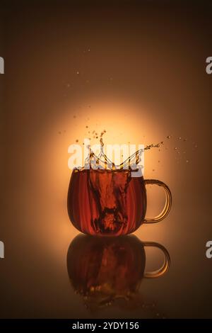 Kreative Splash-Fotografie in transparentem Becher mit Tee, warmen orangen Farben, mit Kopierraum, Komposition Stillleben Stockfoto