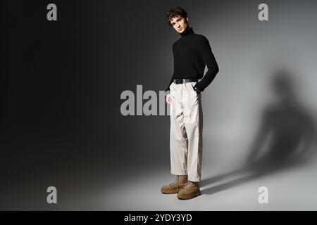 Ein hübscher junger Mann mit lockigen Haaren zeigt ein modernes Outfit auf einem dramatischen dunkelgrauen Hintergrund. Stockfoto