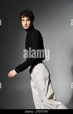 Ein stilvoller junger Mann posiert selbstbewusst auf einem dunkelgrauen Hintergrund und zeigt Eleganz und Mode. Stockfoto