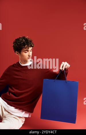 Ein junger Mann mit lockigen Haaren zeigt bunte Einkaufstaschen und feiert den Black Friday in einem lebhaften Studio. Stockfoto