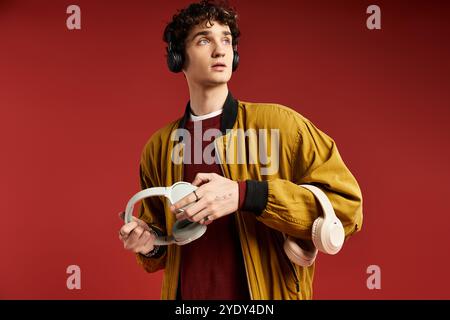 Ein junger Mann mit lockigen Haaren zeigt sein Gespür für Mode, hält Kopfhörer und strahlt Selbstvertrauen aus. Stockfoto