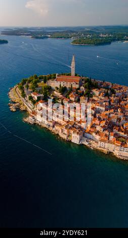 Pulsierende Dächer schmiegen sich an die Küste von Rovinj, Kroatien, während warmes Sonnenlicht die Stadt erfüllt. Das ruhige Meer umgibt die malerische Landschaft und schafft eine ruhige Atmosphäre. Stockfoto