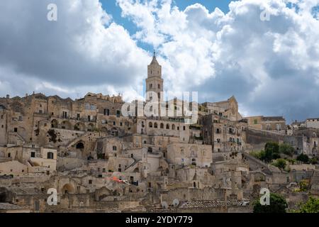 Im Herzen von Apulien, Italien, verzaubert Matera mit seiner antiken Steinarchitektur, einem hohen Glockenturm und einer reichen Geschichte, eingerahmt von wirbelnden Wolken, die zu seinem zeitlosen Charme beitragen. Stockfoto