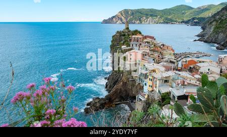 Auf felsigen Klippen gelegen, bieten farbenfrohe Häuser von Cinque Terre Blick auf das azurblaue Wasser, mit üppigen grünen Hügeln, die eine atemberaubende Kulisse für einen malerischen Tag bieten, Vernazza Italien Stockfoto