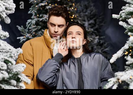 Ein wunderschönes Paar steht eng zusammen und strahlt Wärme und Liebe in der Nähe von schneebedeckten Kiefern aus. Stockfoto