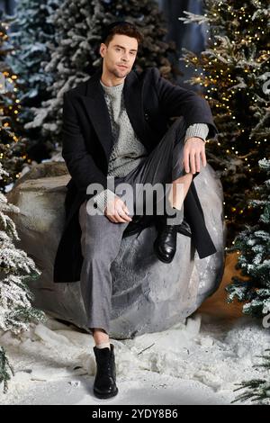 Ein fröhlicher Mann in Winterkleidung genießt die festliche Atmosphäre, umgeben von schneebedeckten Kiefern. Stockfoto