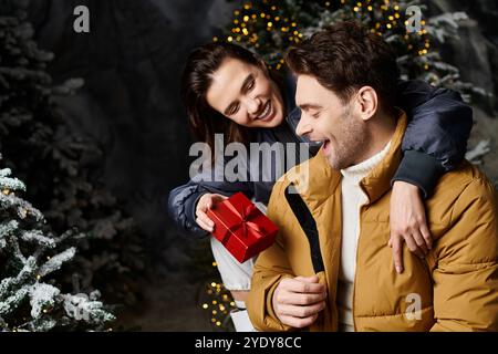 Ein Paar in stilvollen Winterjacken teilt einen freudigen Moment und tauscht Weihnachtsgeschenke im Schnee aus. Stockfoto