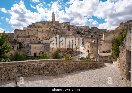 Wandern Sie durch die historischen Gassen von Matera in Apulien, Italien, wo alte Steinhäuser sich gegen einen atemberaubenden Himmel erheben, der mit flauschigen Wolken geschmückt ist. Stockfoto
