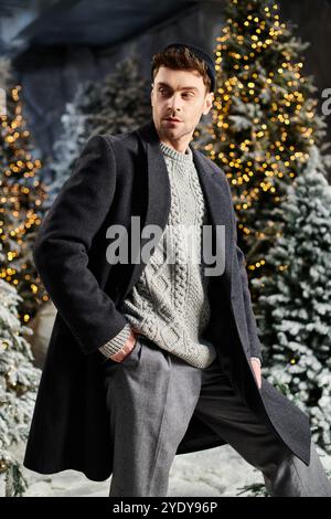 Ein gutaussehender Mann in Winterkleidung steht selbstbewusst in der Nähe von schneebedeckten Kiefern und fängt den Urlaubsgeist ein. Stockfoto