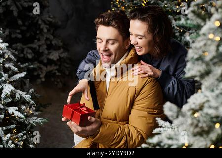 Ein glückliches Paar genießt einen gemütlichen Moment in der Nähe von schneebedeckten Kiefern und feiert die Liebe und den Zauber von Weihnachten. Stockfoto