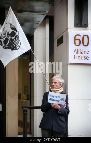 London, England, Großbritannien. Oktober 2024. Ein Demonstrant demonstriert vor den Büros der Allianz Versicherungsgesellschaft mit einem Schild mit der Aufschrift ''˜boykott Allianz'. Extinction Rebellion (XR) spazieren Sie durch die City of London, halten Sie an und demonstrieren Sie vor den Büros von Versicherungsunternehmen, die trotz der Warnungen vor einer Klimakrise von Wissenschaftlern weiterhin Unternehmen für fossile Brennstoffe versichern. Die Demonstranten glauben, wenn die Versicherungsgesellschaften ihre Beteiligung an diesen Unternehmen beenden würden, würden sie es schwer tun, weiter zu bauen. Die Aktion ist die erste einer Woche lang, die sich speziell gegen den Protest richtet Stockfoto