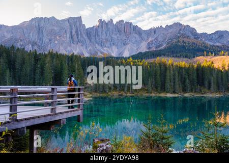 Ein einsamer Wanderer steht auf einer hölzernen Plattform und genießt bei Sonnenaufgang die atemberaubende Aussicht auf die Dolomiten. Karersee oder Karersee Dolomiten in Italien. Stockfoto