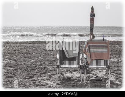 Zwei Liegestühle nebeneinander an einem leeren Strand in Vintage-Farben, die Feiertage und die Liebe zu einem älteren Paar im Ruhestand repräsentieren Stockfoto