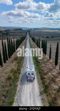 Auf einer staubigen Straße, die von hohen Zypressen flankiert wird, entfaltet sich eine sanfte Reise in die atemberaubende toskanische Landschaft. Die Szene fängt das Wesen des ländlichen Italiens ein und lädt zu Abenteuern und Ruhe ein. Stockfoto