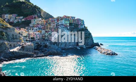 Ein malerisches Dorf umgibt die Klippen von Cinque Terre, dessen lebhafte Gebäude sich im klaren blauen Mittelmeer-Wasser spiegeln. Manarola in Cinque Terre Italien Stockfoto