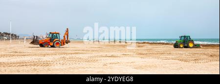 Arbeiter verwenden Traktoren, um Algen zu entfernen und den Sandstrand für Besucher an einem hellen Tag vorzubereiten. Stockfoto