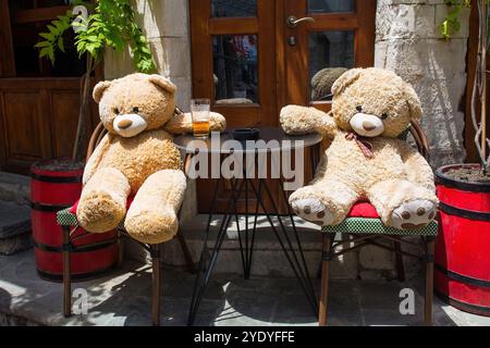 Zwei riesige Teddybären genießen ein Bier vor einer Bar im Gjirokaster Basar, einem historischen Marktplatz, der für seine gut erhaltene osmanische Architektur bekannt ist. Stockfoto