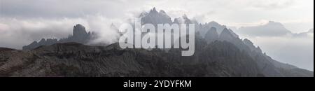 Ein dramatisches, nebelbedecktes Panorama der zerklüfteten Gipfel von Cadini di Misurina in den italienischen Dolomiten, vor einem bewölkten, atmosphärischen Himmel Stockfoto