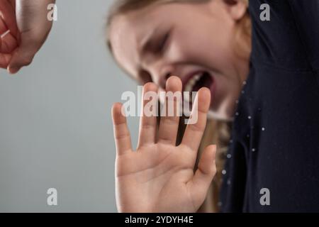 Ein junges Mädchen schreiend mit geschlossenen Augen, während sie ihre Hand in einer Verteidigungsgeste hebt und Angst, Angst und das Bedürfnis nach Schutz vor ausdrückt Stockfoto