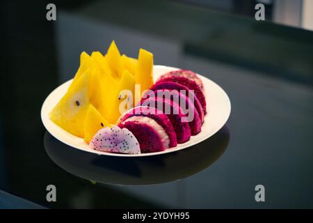 Scheiben von Drachenfrüchten und eine gelbe Wassermelone auf einem weißen Teller auf einem schwarzen Tisch. Stockfoto