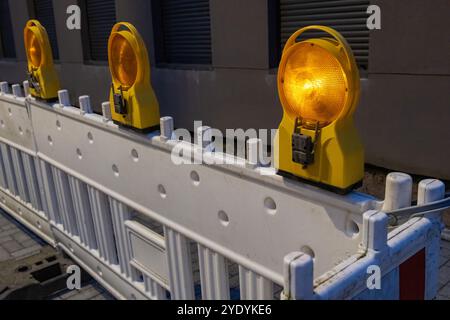 Blinkende gelbe Rundlichter an weißer Straßensperre bei Nacht, um eine Baustelle zu schützen und den Verkehr abzulenken Stockfoto