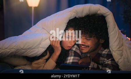 Gadget Internet-süchtig multirassisches Paar glückliche Familie Mann Frau Freund Freundin in der Nacht zu Hause unter der Decke, die ekelhafte schlechte Nachrichten Video Stockfoto