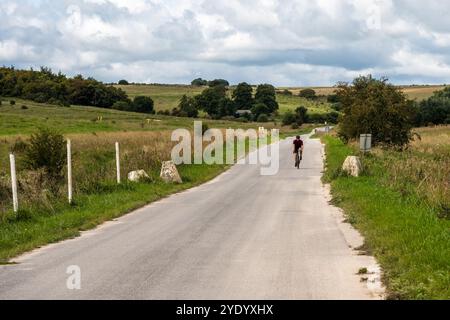 Ein Radfahrer fährt an Warnschildern vorbei auf einer Straße durch die Imber Ranges, dem Trainingsgebiet der British Army auf der Salisbury Plain in Wiltshire, England. Stockfoto