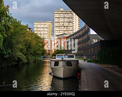 Die Boote liegen am Paddington Arm des Grand Union Canal unter der Westway Road in West London, wobei die Turmblöcke des Brindley Estate behi aufsteigen Stockfoto