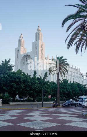 Eine große, weiße, reich verzierte Kathedrale namens „sacré coeur“ mit zwei hohen Türmen, umgeben von üppigen grünen Bäumen und Palmen, mit einem karierten Pflaster Stockfoto